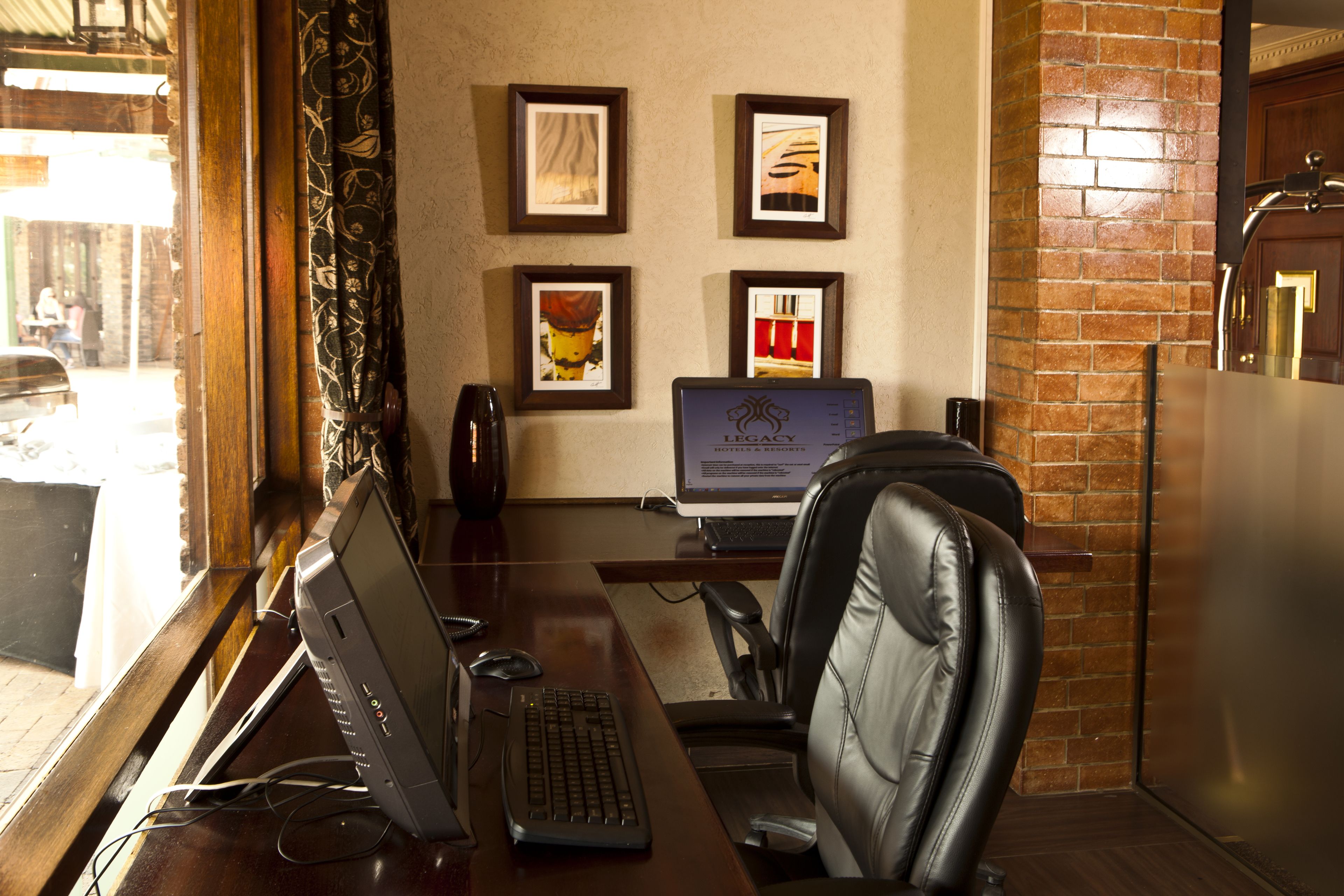 Habitación de hotel con escritorio, ordenador y sillón de cuero. Se observan cuadros enmarcados en la pared y una pared decorativa de ladrillo.