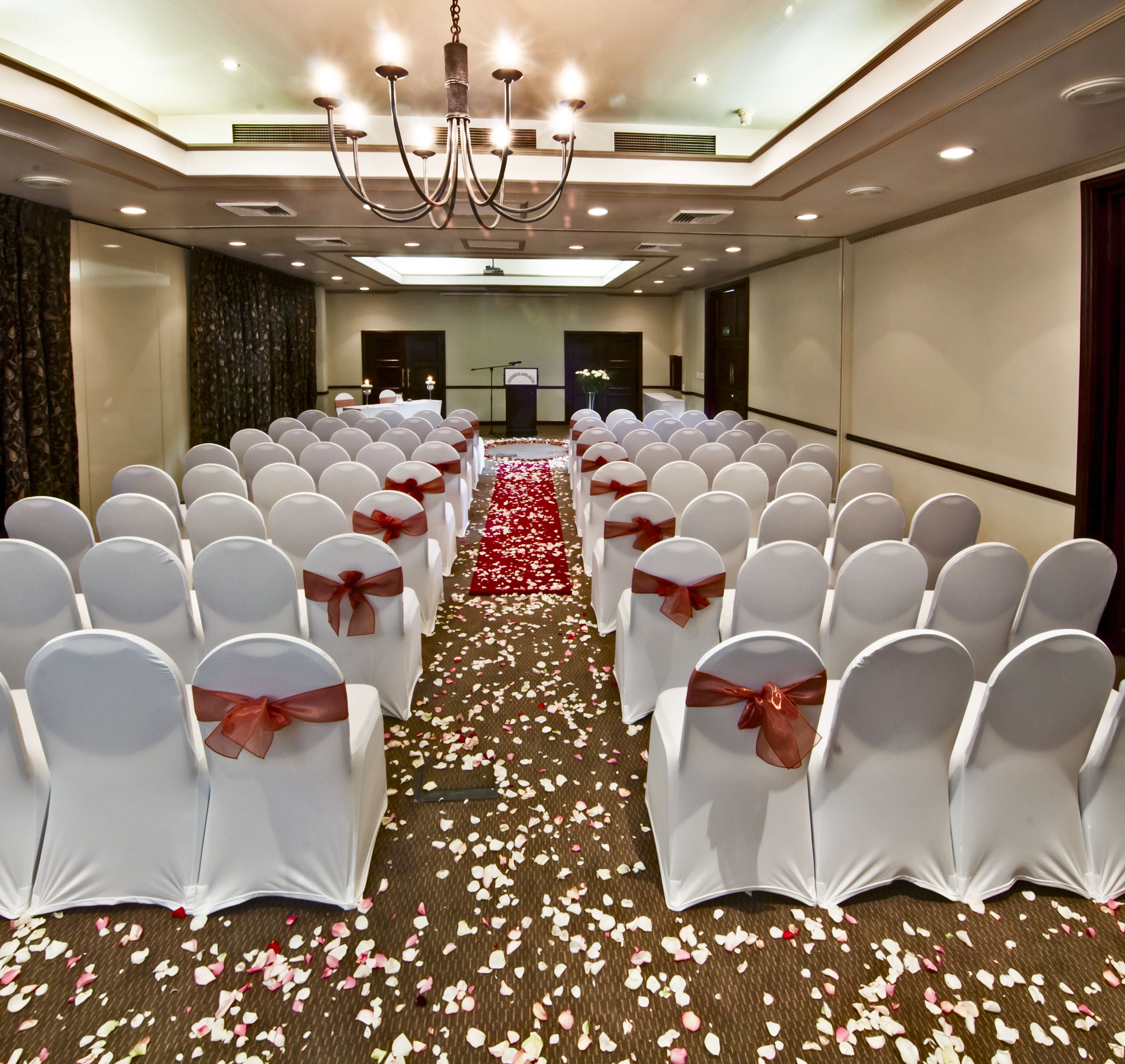 A conference room with rows of white chairs, a red carpet, and a chandelier.