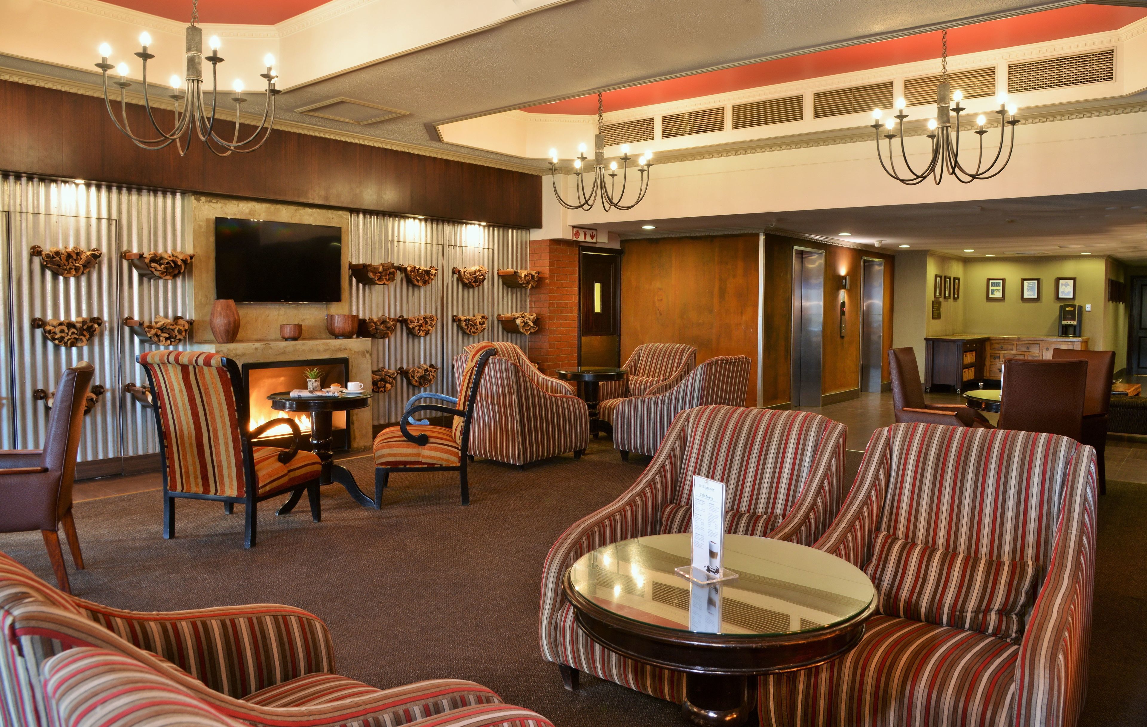 A lobby with striped sofas, a fireplace, a TV, and a chandelier.