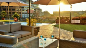 Un patio con mobiliario de mimbre, dos sombrillas y una piscina al fondo.
