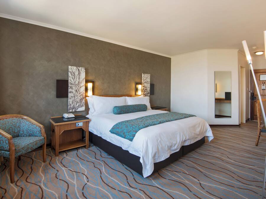 A hotel room with a large bed, a nightstand, a chair, and a mirror.