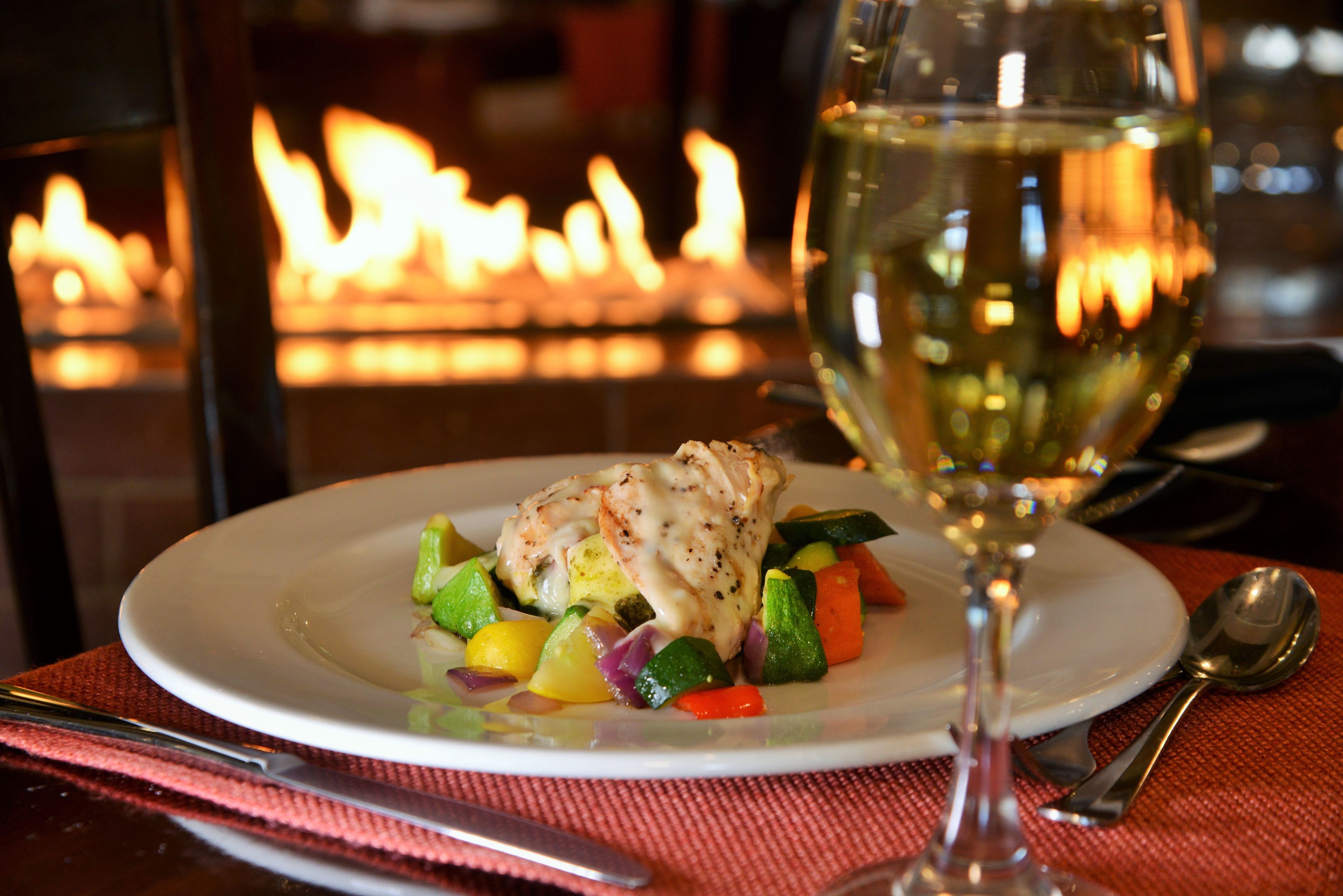 Ein Teller mit Essen und ein Glas Weißwein auf einer Tischplatte mit roter Unterlage.