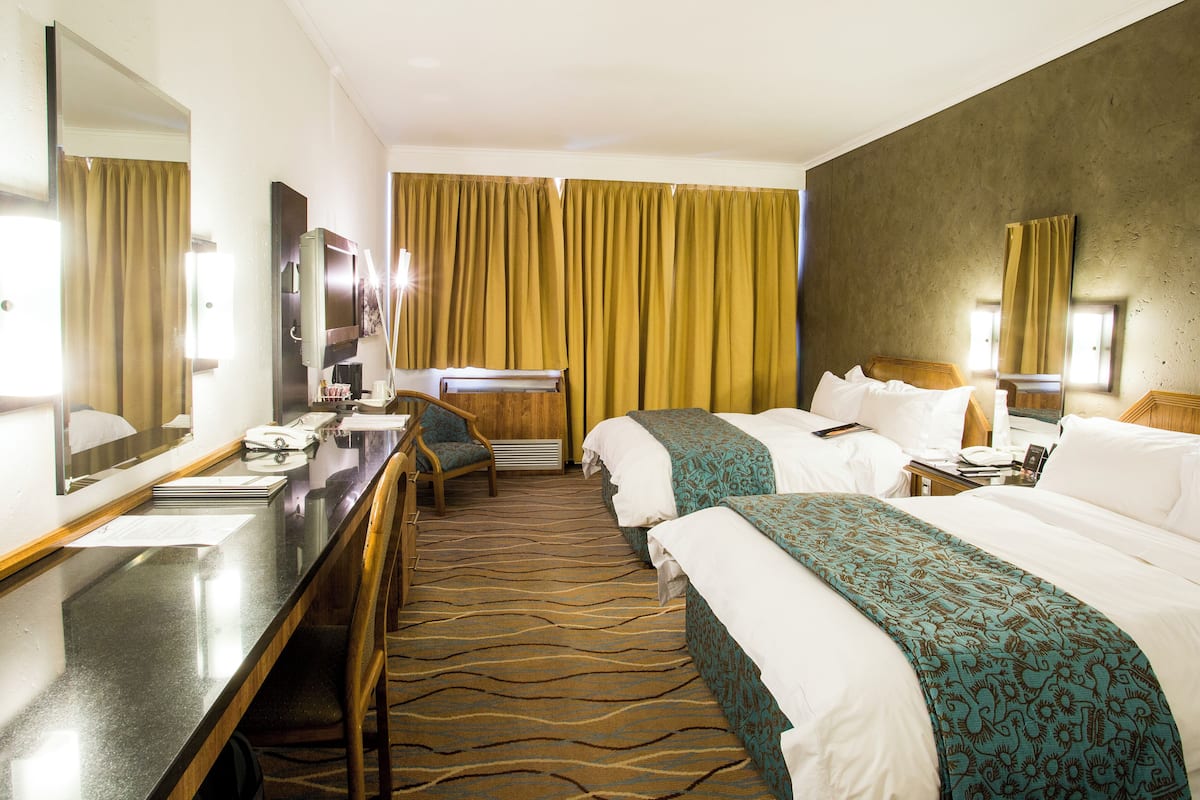 Ein Hotelzimmer mit Bett, Schreibtisch, Stuhl, Spiegel, Fenster mit Vorhängen und Teppich.