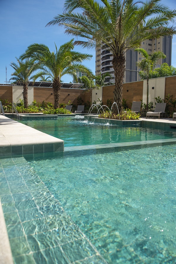 Una piscina al aire libre, sombrillas, sillones reclinables de piscina