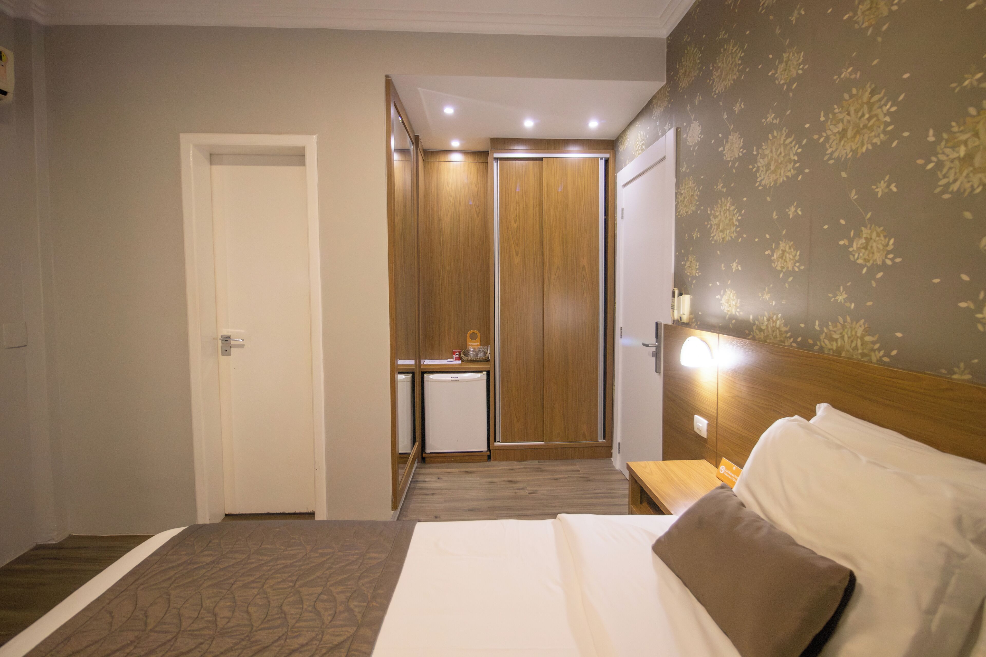 A hotel room with a bed, a small kitchenette, a wardrobe, and a bathroom.