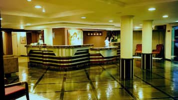 A hotel lobby with a reception desk, seating area, and a large window.