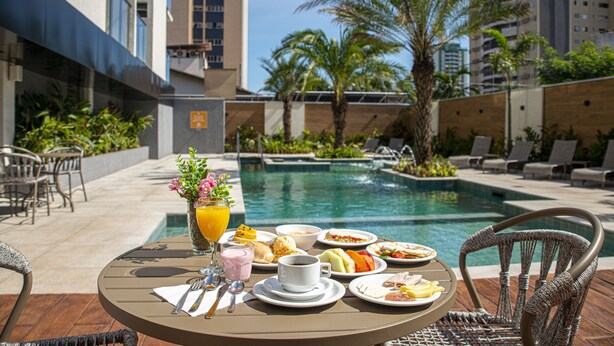 Una mesa de comedor con alimentos para el desayuno y una piscina al fondo.