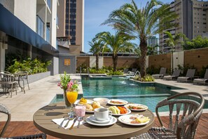A dining table with breakfast items and a pool in the background.