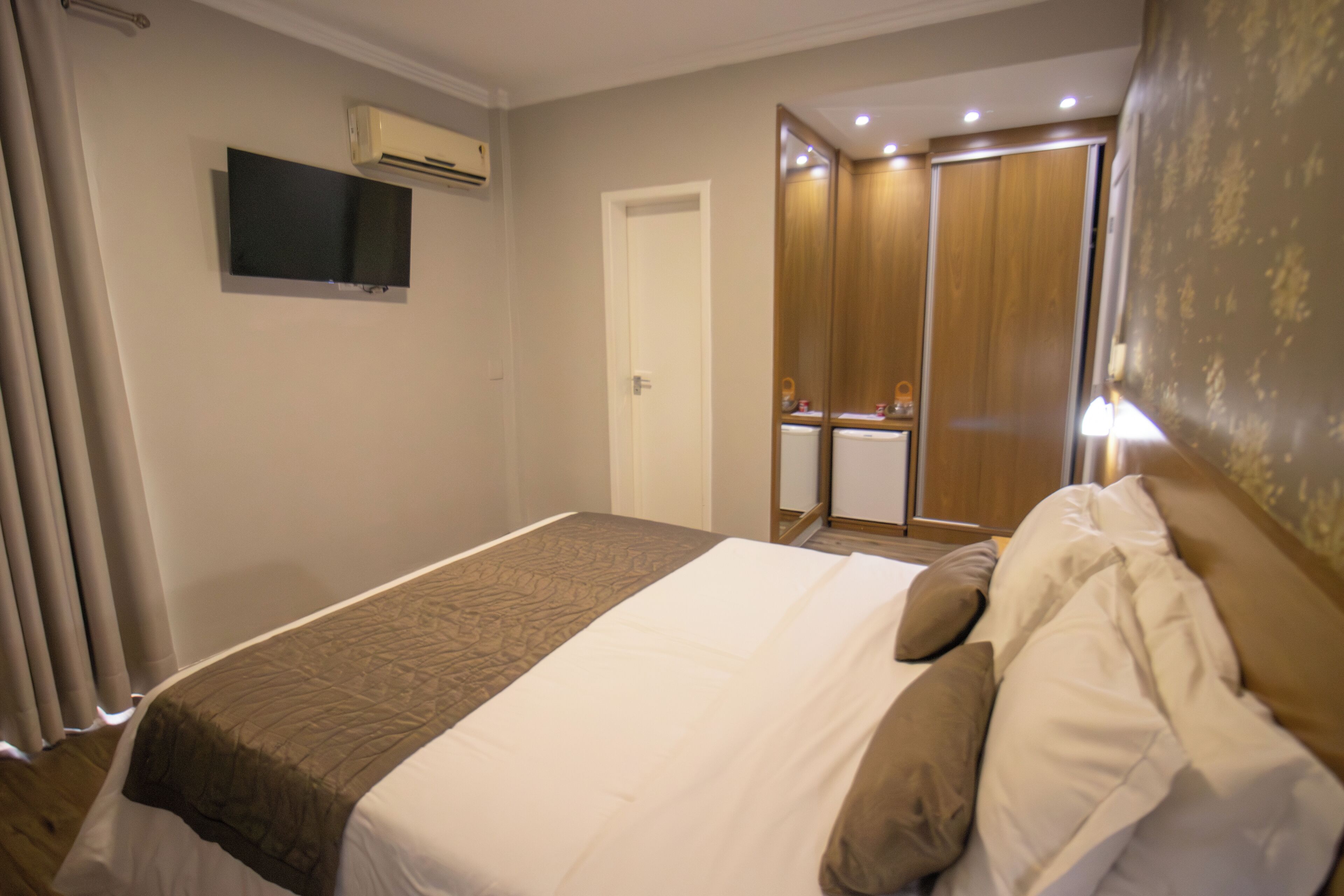 A hotel room with a bed, a television mounted on the wall, and a wardrobe with a mirror.
