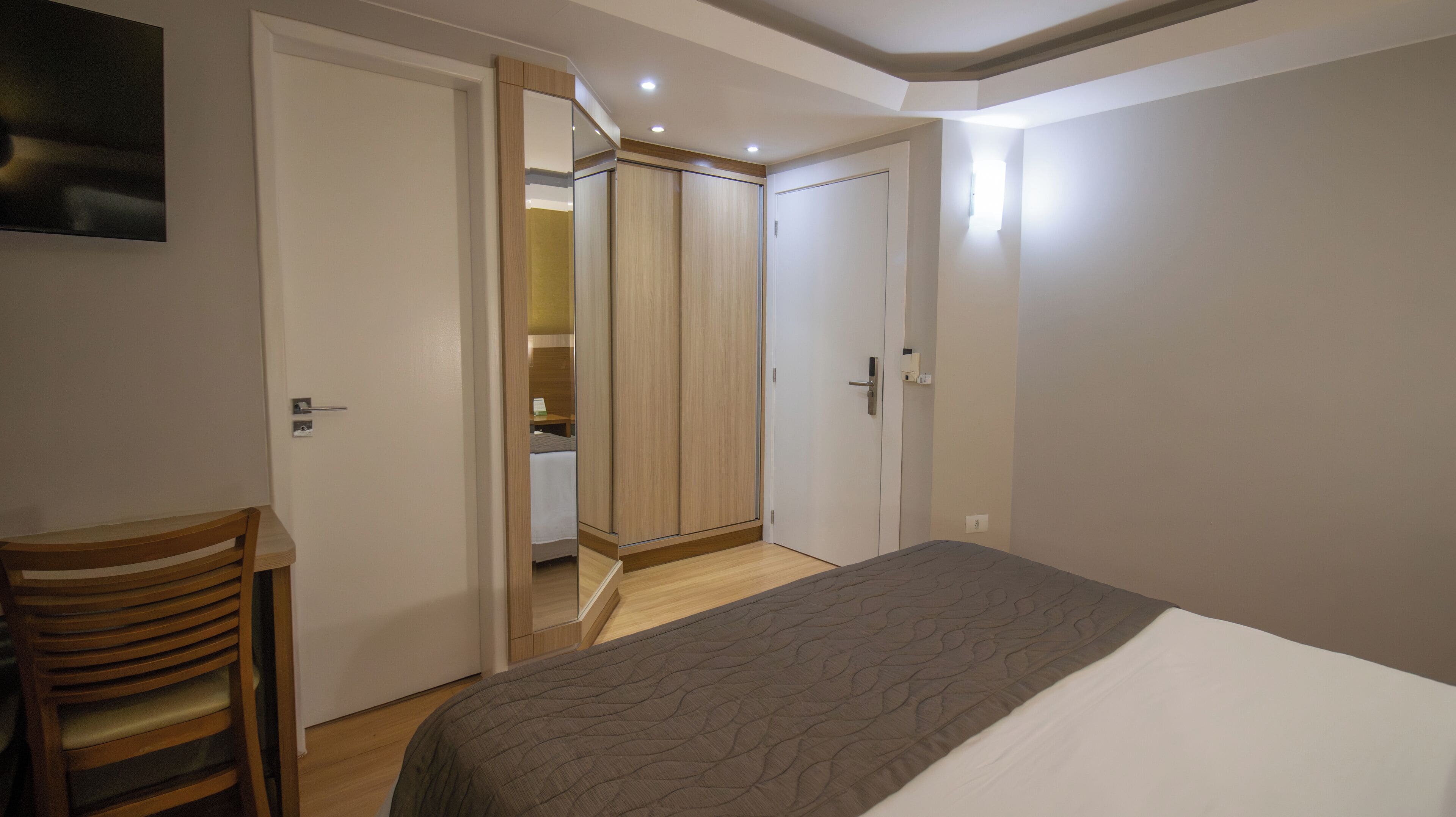 A bedroom with a bed, a wooden chair, a wardrobe, and a mirror.