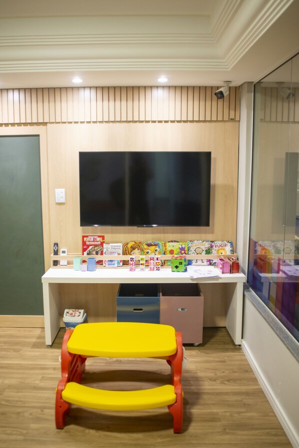 A room with a wooden desk, a television mounted on the wall, and a small yellow stool in front.