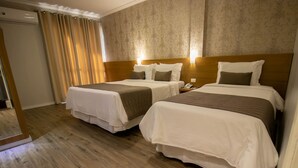 Habitación de hotel con dos camas, suelo de madera, papel tapiz estampado y una cortina.