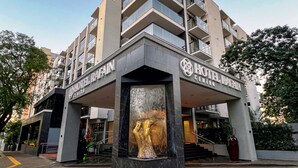 Un hotel de varios pisos con fachada moderna, que cuenta con grandes ventanales y una entrada central con una escultura de mármol.