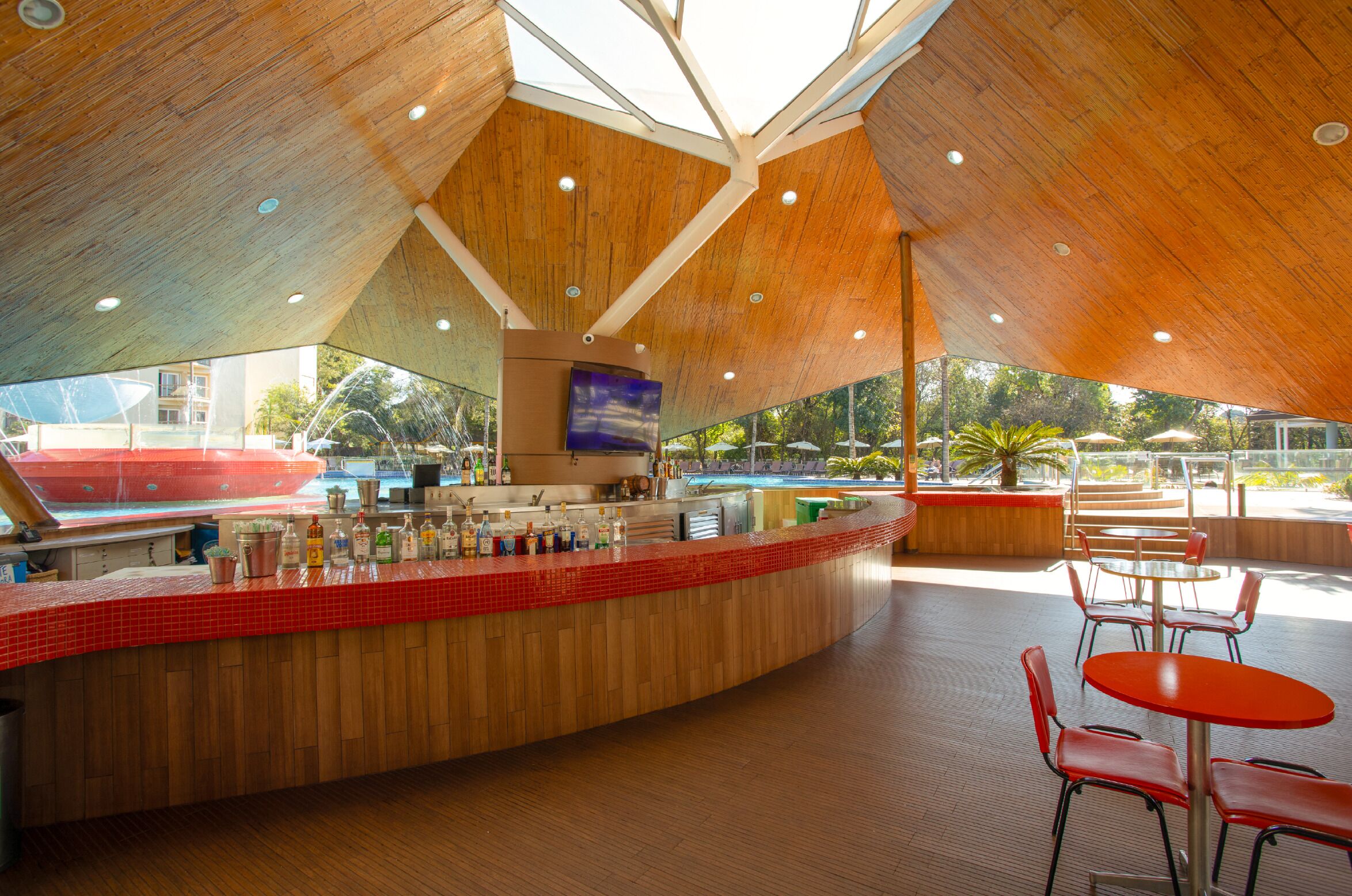 A modern bar area with a wooden ceiling, a red-tiled counter, and outdoor seating.