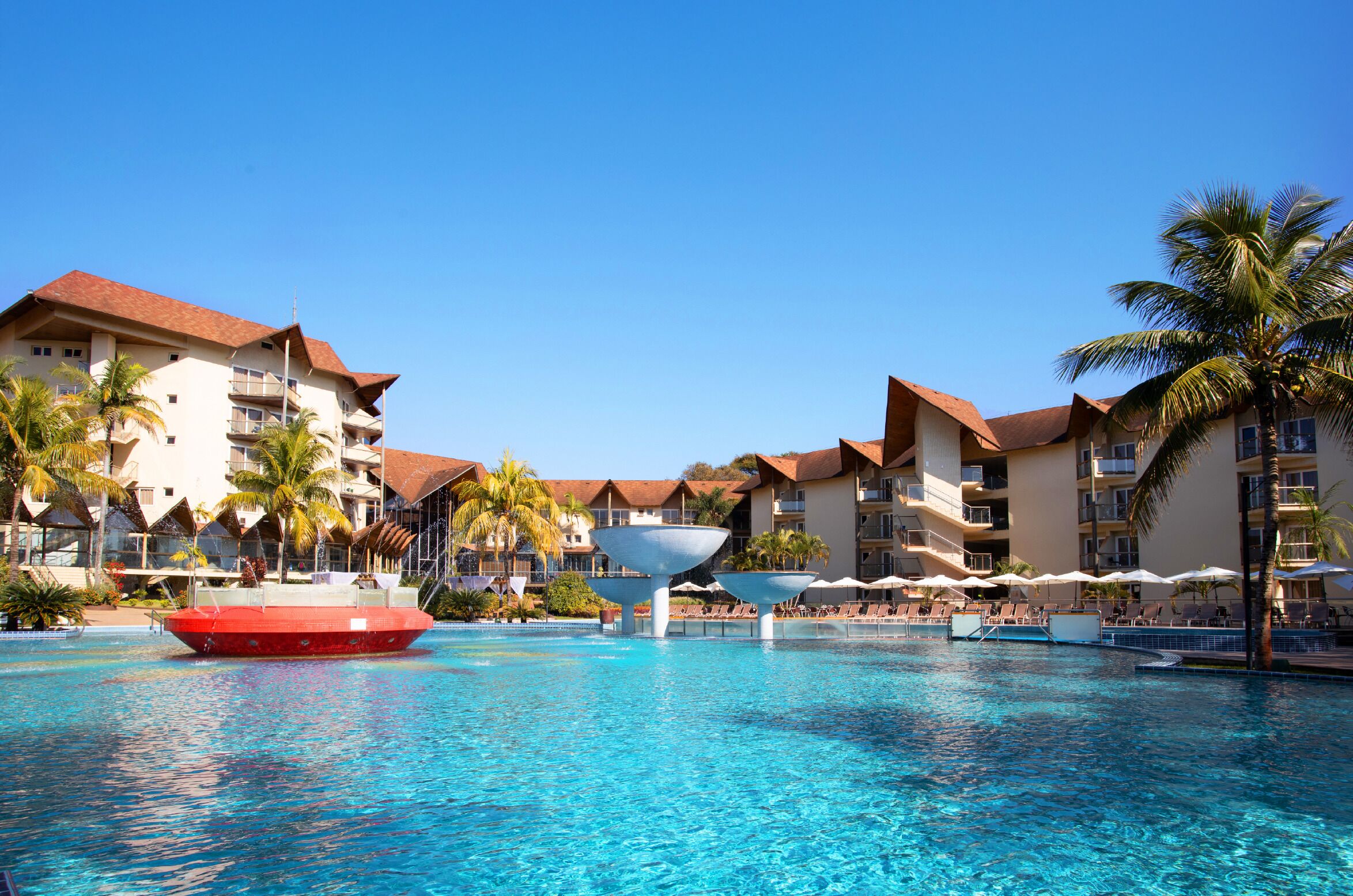 A hotel with a swimming pool, palm trees, and a red boat.