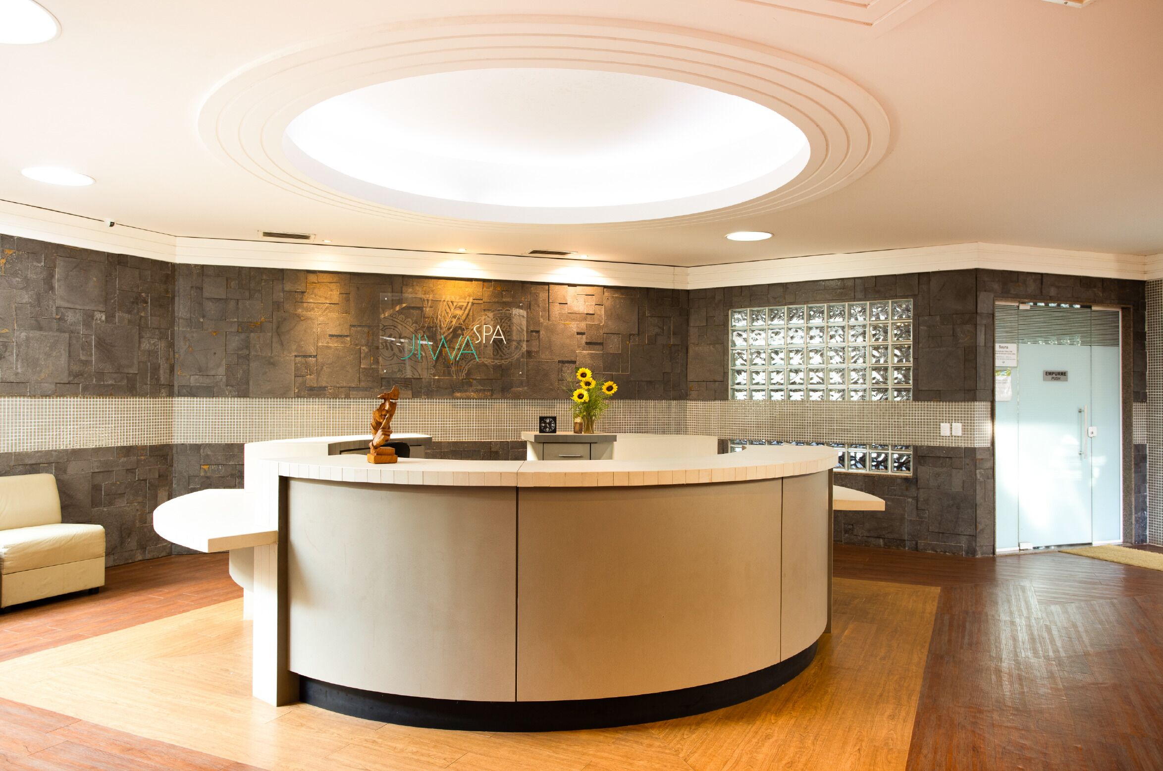 A reception area with a curved counter, a sofa, a wall with a stone pattern, and a ceiling with circular lighting.