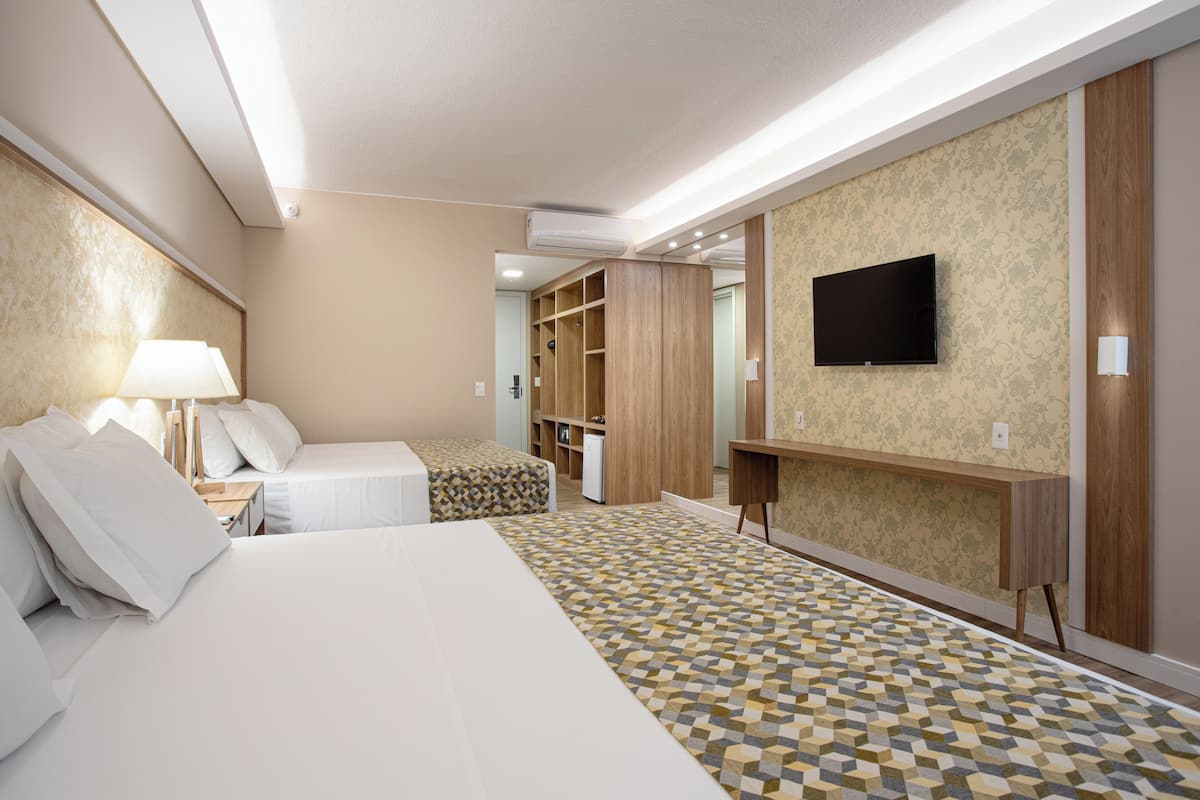 Une chambre d’hôtel avec un lit, un bureau, une télévision, une armoire et un sol à motifs.
