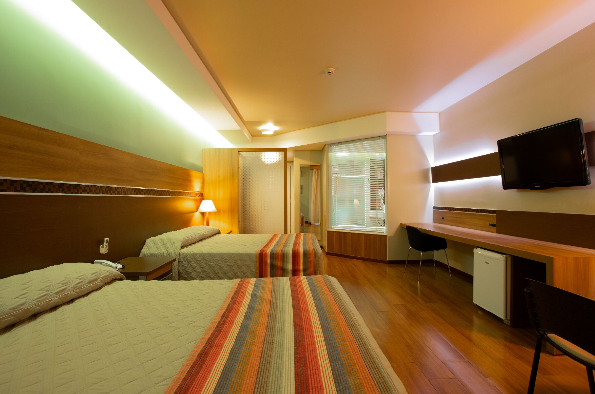 A hotel room with two beds, a desk, a television, and a small refrigerator.