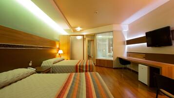 A hotel room with two beds, a desk, a television, and a small refrigerator.