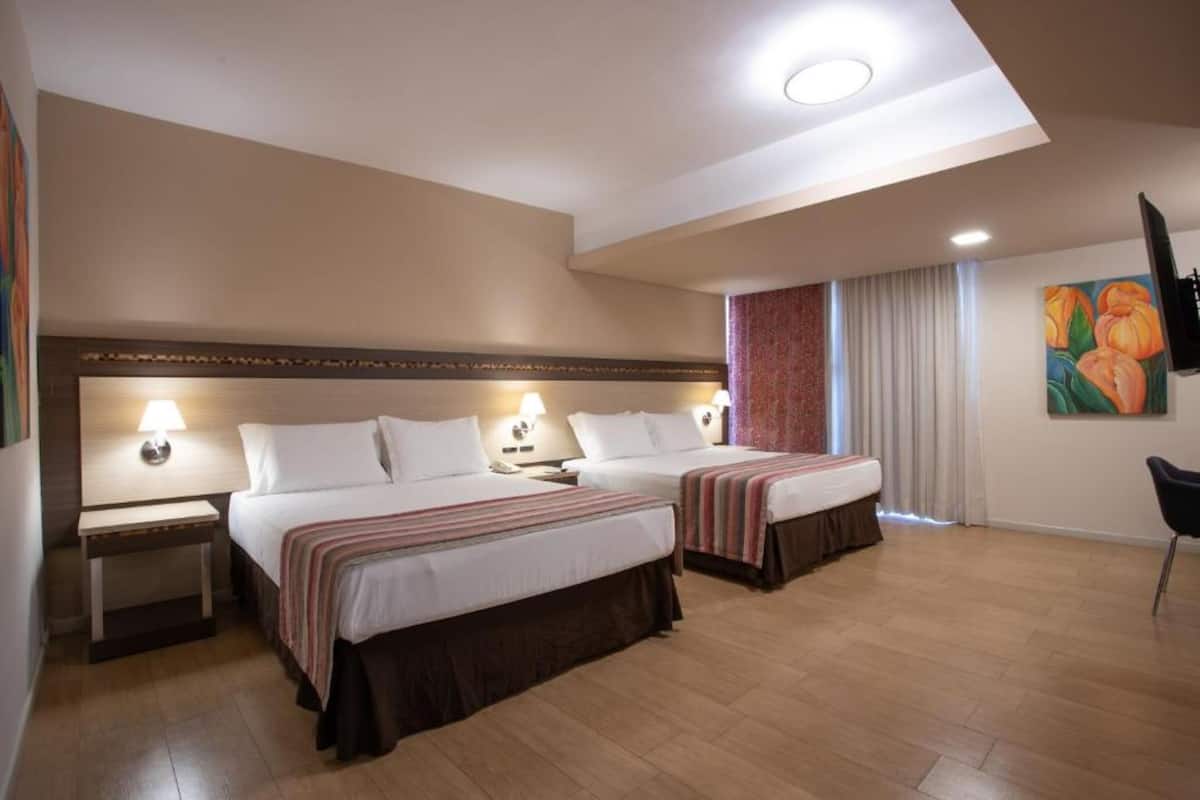 Une chambre d’hôtel avec deux lits, un bureau, une télévision et un tableau au mur.