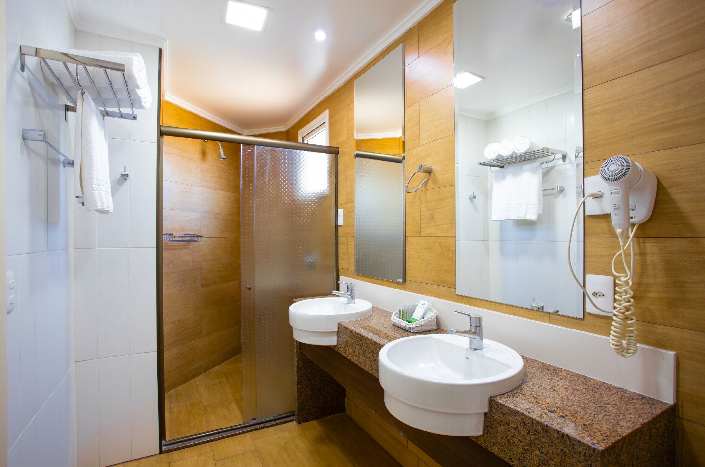 Un baño moderno con dos lavamanos, cabina de ducha de vidrio, secador de pelo y toallero.