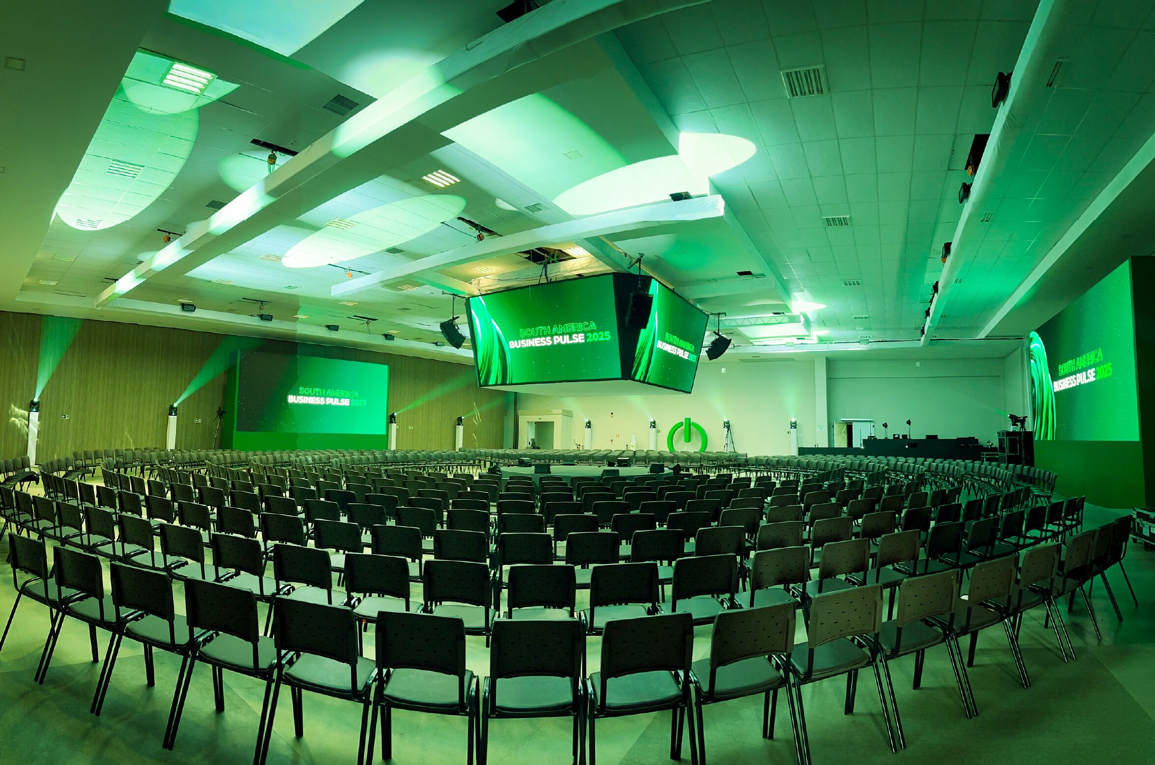 Una sala conferenze con file di sedie, un grande schermo che mostra 'South America Business Pulse 2025' e un palco con un podio.