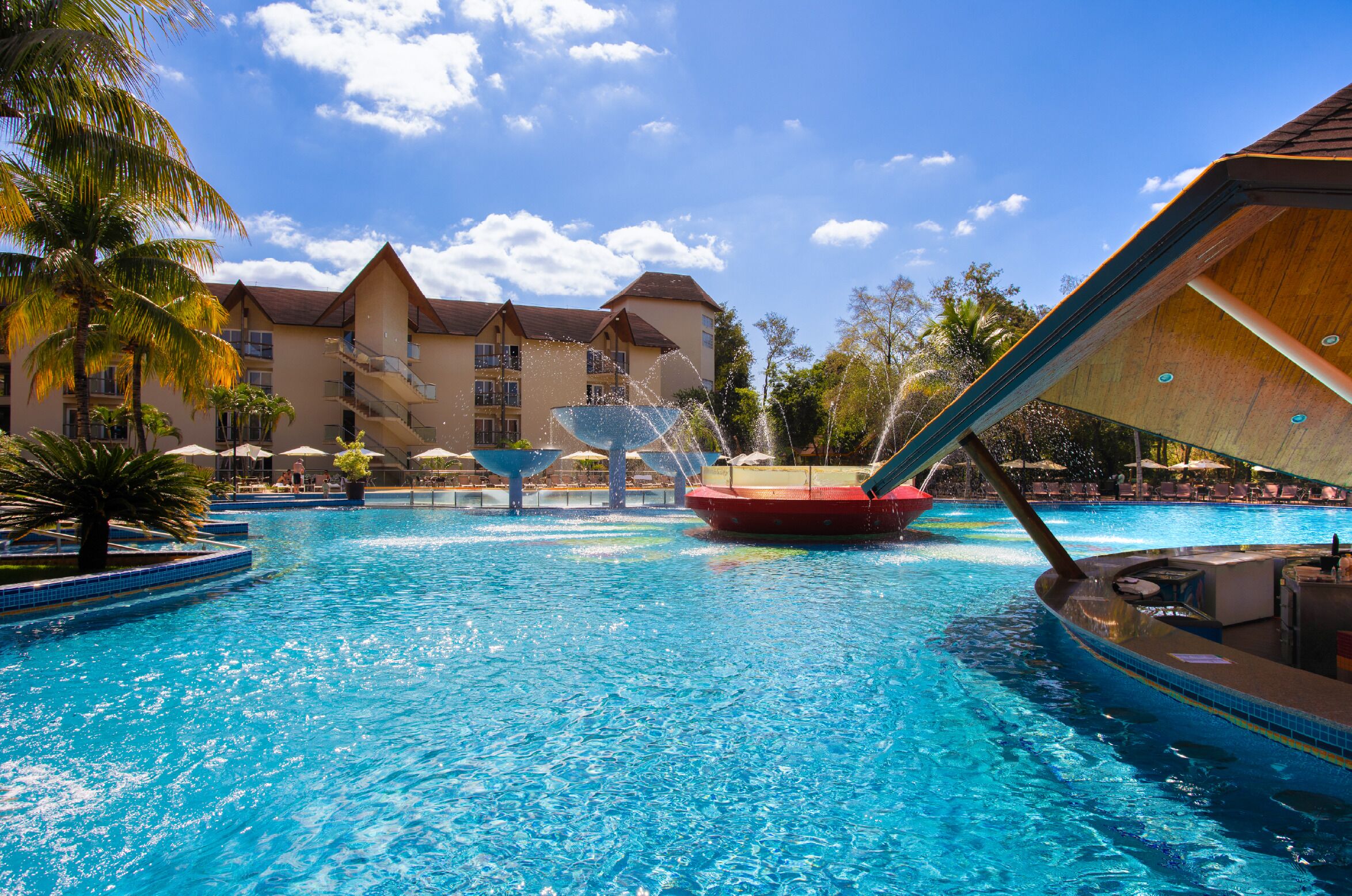 A swimming pool with a water slide, palm trees, and a building with multiple balconies.