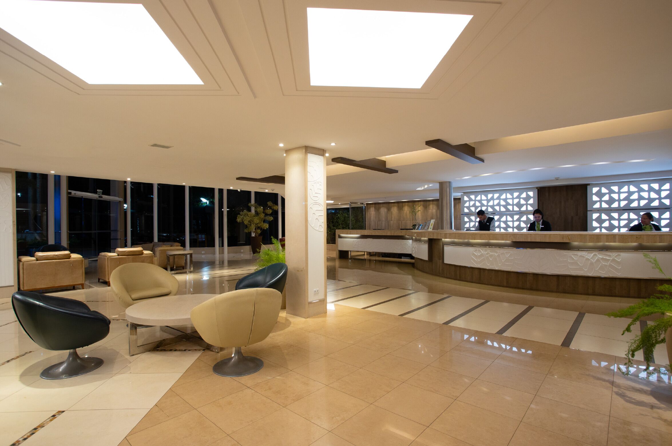 A modern hotel lobby with a reception desk, seating area, and large windows.