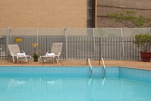 Una piscina con dos sillas de descanso y una planta en maceta.