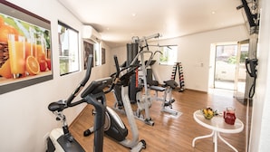 Un gimnasio con máquinas de cardio, una pequeña mesa con fruta y una bebida, y un cuadro de fruta en la pared.