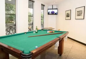 A pool table with balls, a television mounted on the wall, and framed pictures on the wall. - Royal Center Lourdes (Belo Horizonte)