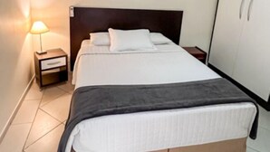 Un letto rifatto con cura, una testiera scura, un comodino con una lampada e un armadio a due ante.