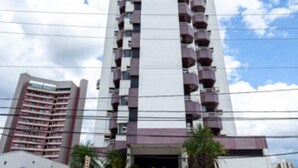 Un edificio alto con una scalinata centrale che conduce all'ingresso, circondato da piante in vaso e un cielo sereno.