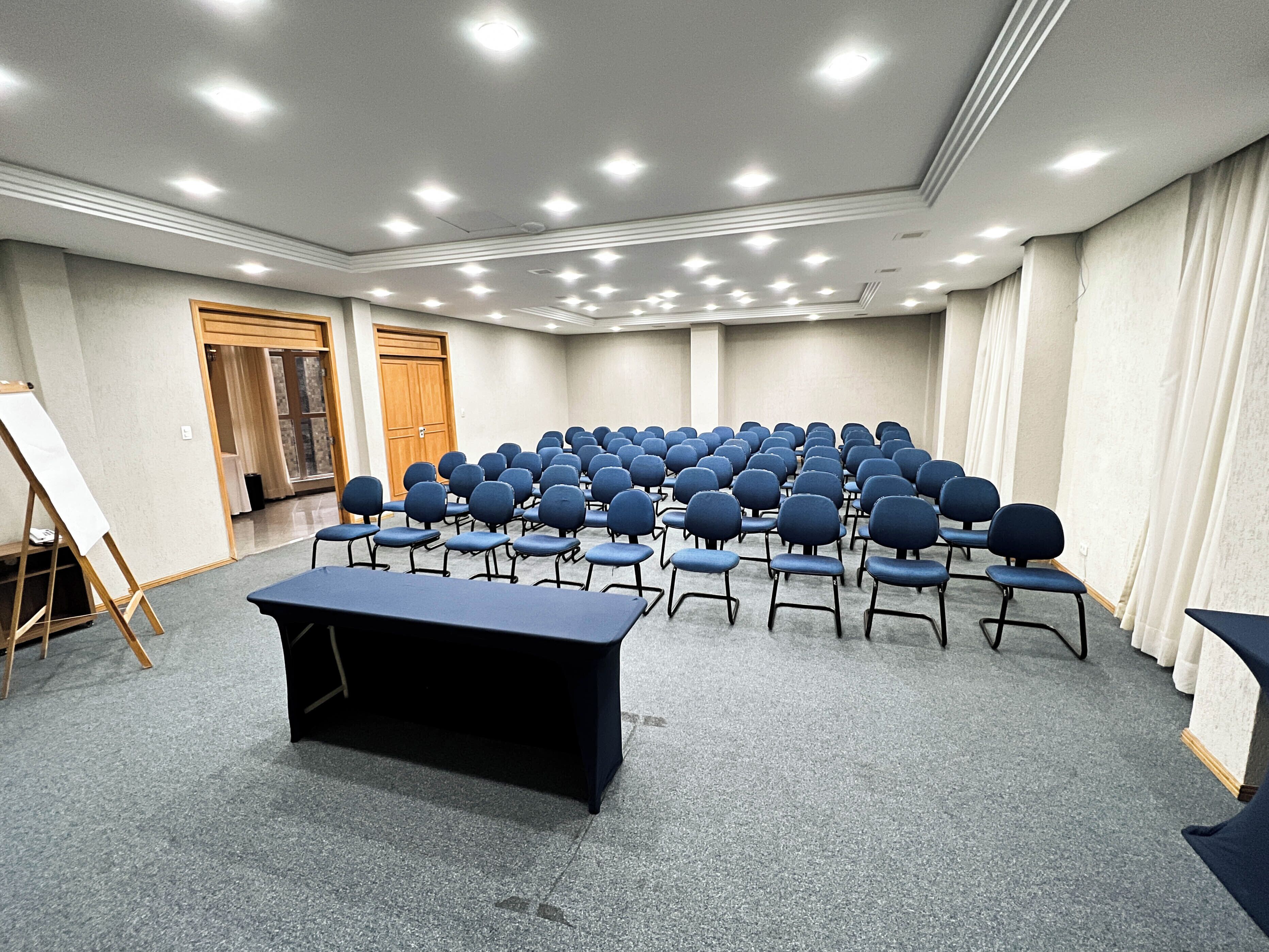 Un salón de conferencias con filas de sillas, una mesa y una pizarra.
