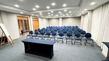 Un salón de conferencias con filas de sillas, una mesa y una pizarra.