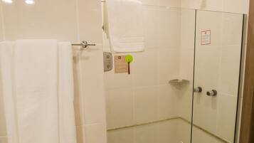 Um chuveiro com paredes de vidro, uma toalha branca pendurada em um porta-toalhas, uma porta de vidro e piso revestido com azulejos.
