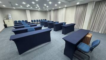 Un salón de conferencias con varias mesas y sillas, un atril y un pequeño armario con dispensador de agua.