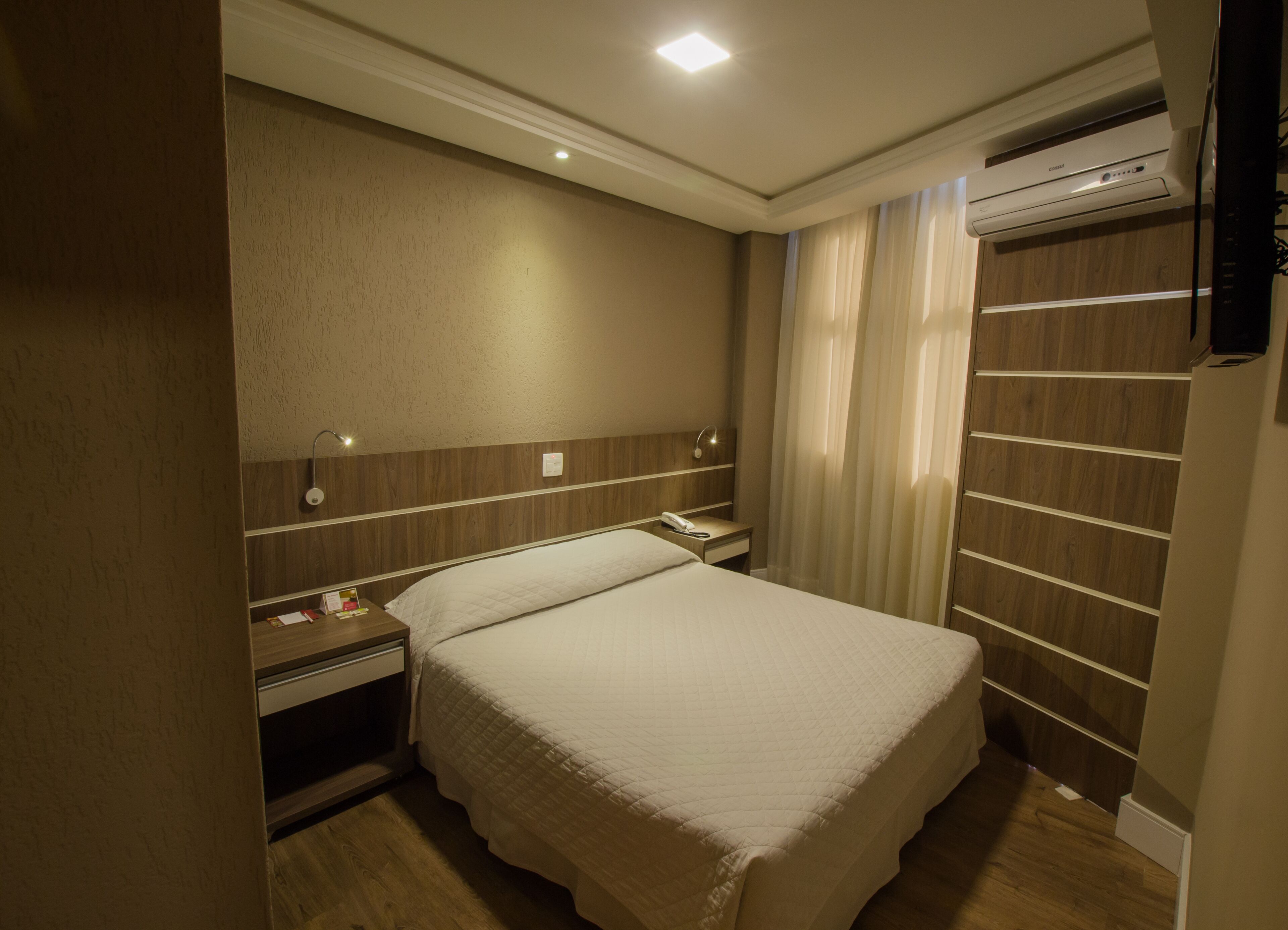 Ein Hotelzimmer mit Bett, Nachttisch, Lampe und Klimaanlage.