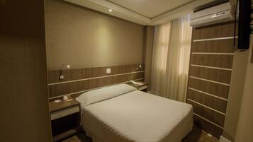 Habitación de hotel con cama, mesita de noche, lámpara y unidad de aire acondicionado.