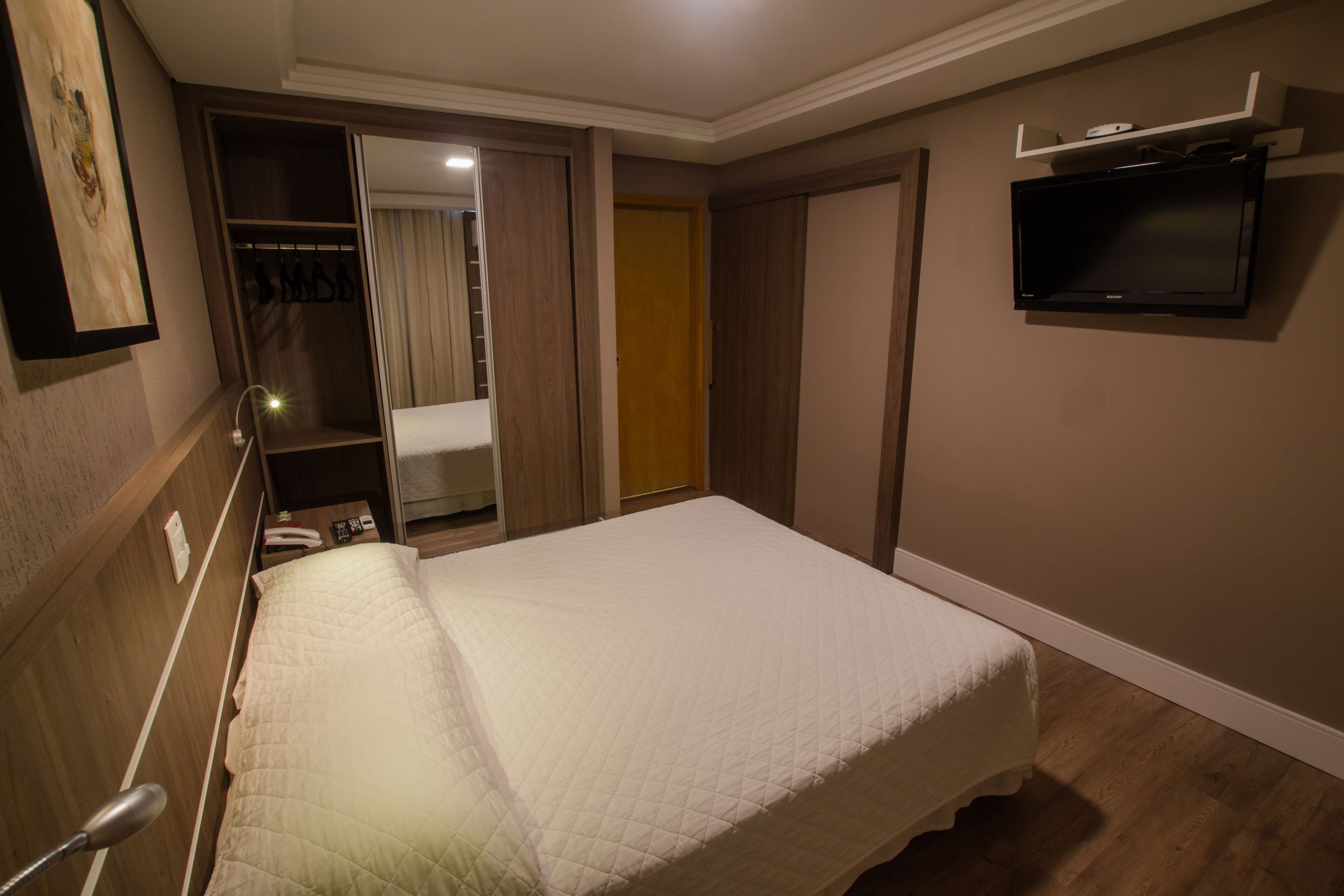 A bedroom with a bed, a wardrobe, a television, and a bathroom visible through an open door.