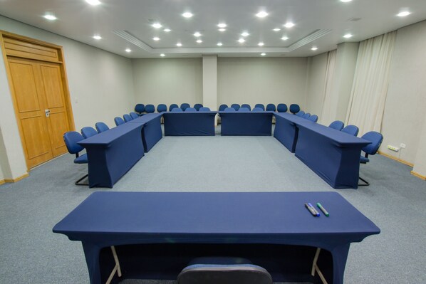 Un salón de conferencias con una larga mesa y sillas, una puerta de madera y una cortina en un lateral.