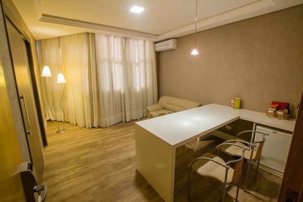 A modern hotel room with a wooden floor, a white dining table with bar stools, a sofa, and a large window with curtains. - SJ Royal - San Juan Curitiba (Curitiba)