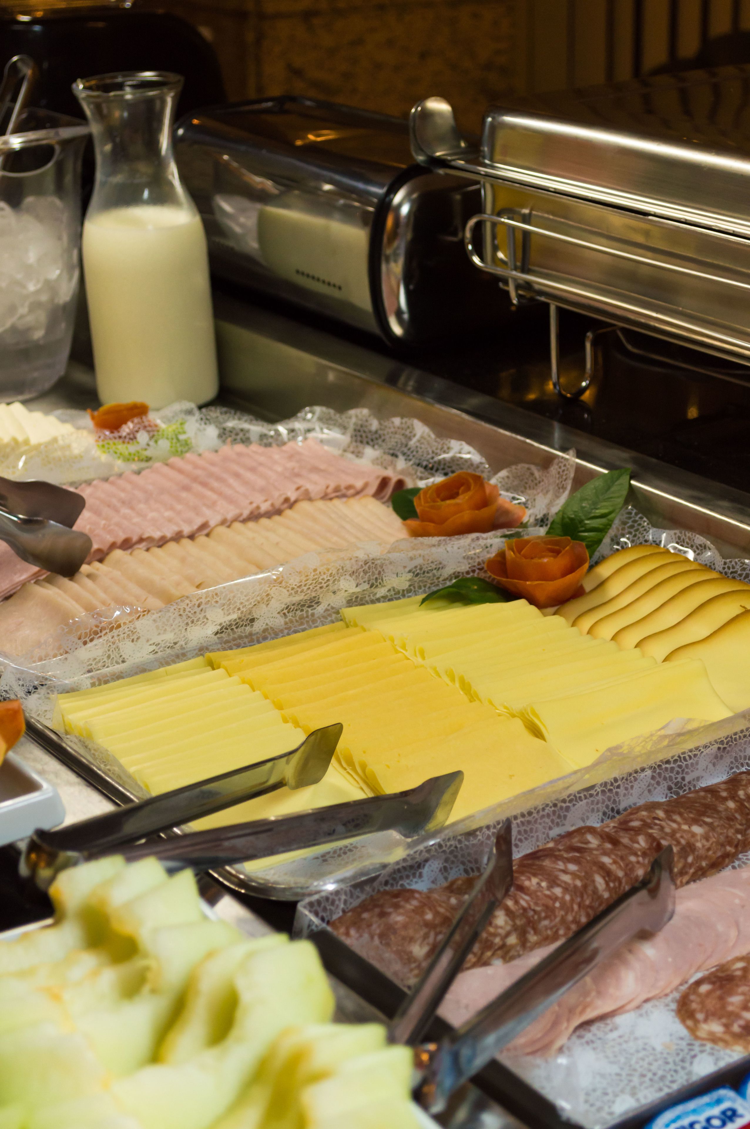 A buffet with various food items including sliced meats, cheeses, and a milk dispenser.