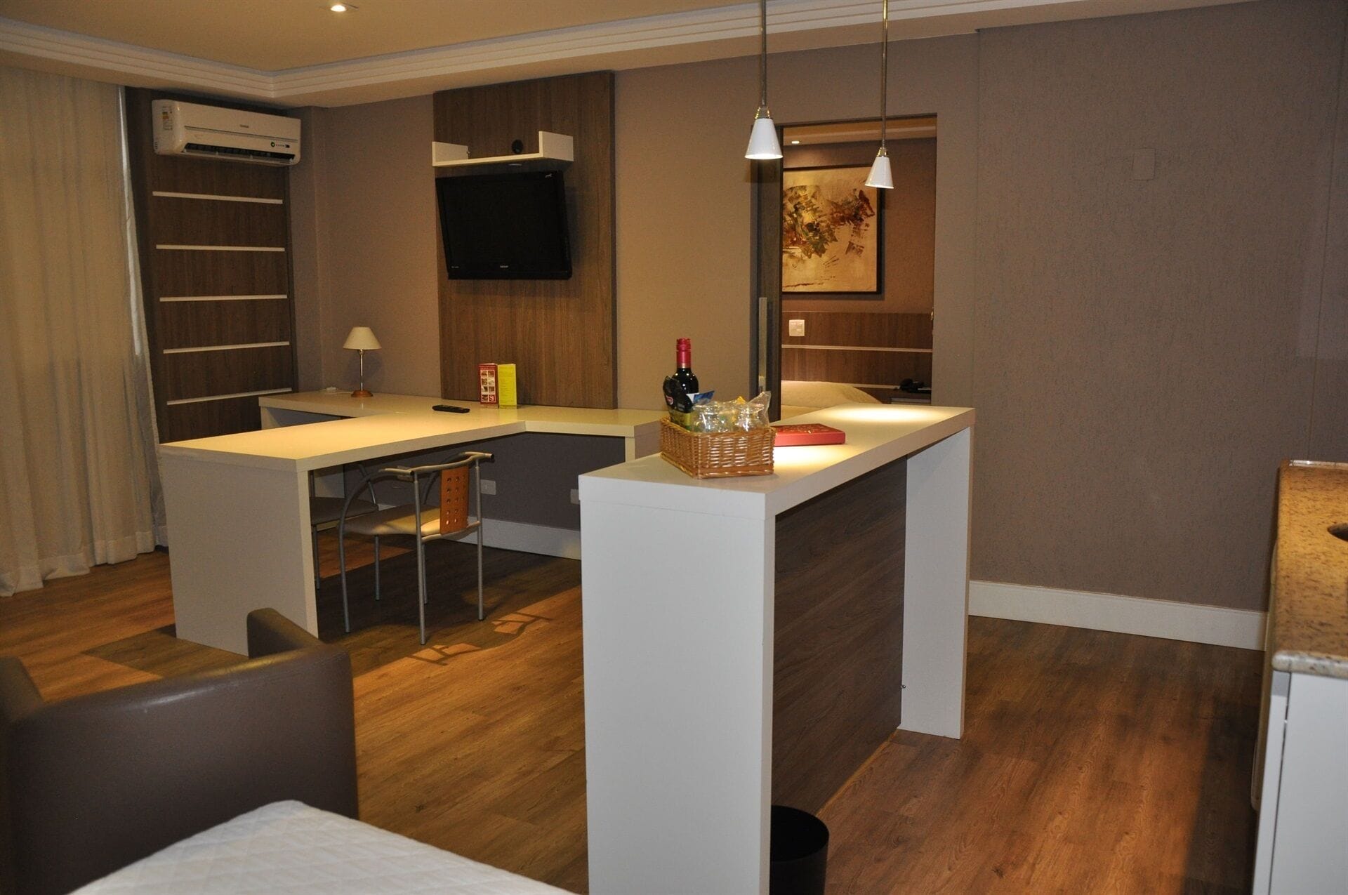 A compact hotel room with a kitchenette, a flat-screen TV, a dining area, and a bed.