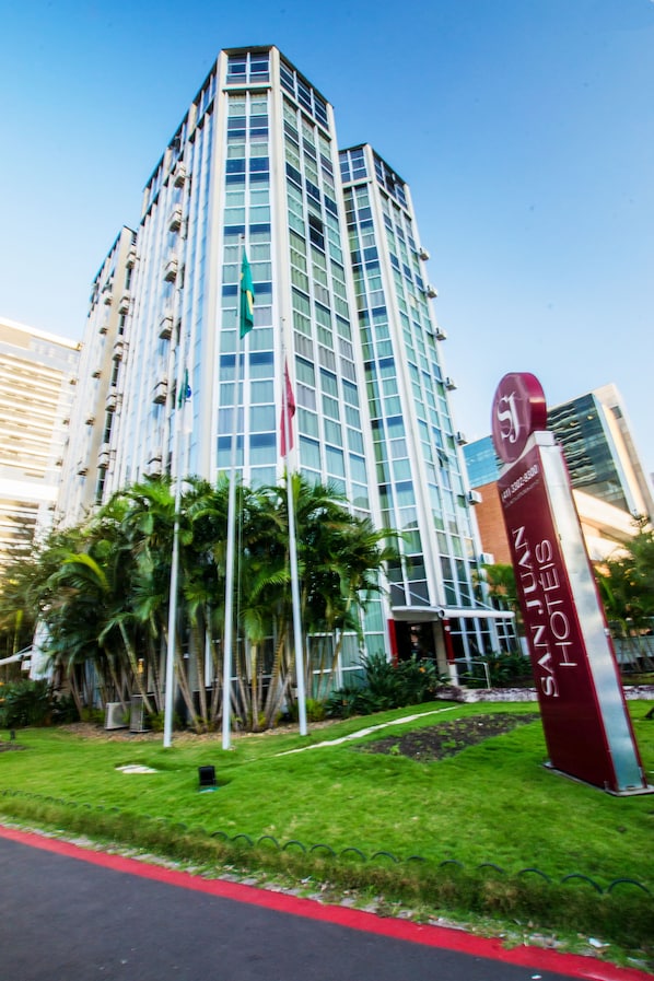 A tall hotel building with a modern glass facade, a prominent entrance sign, and surrounding greenery.
