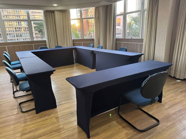 Une salle de conférence avec une longue table, des chaises bleues et de grandes fenêtres dotées de rideaux.