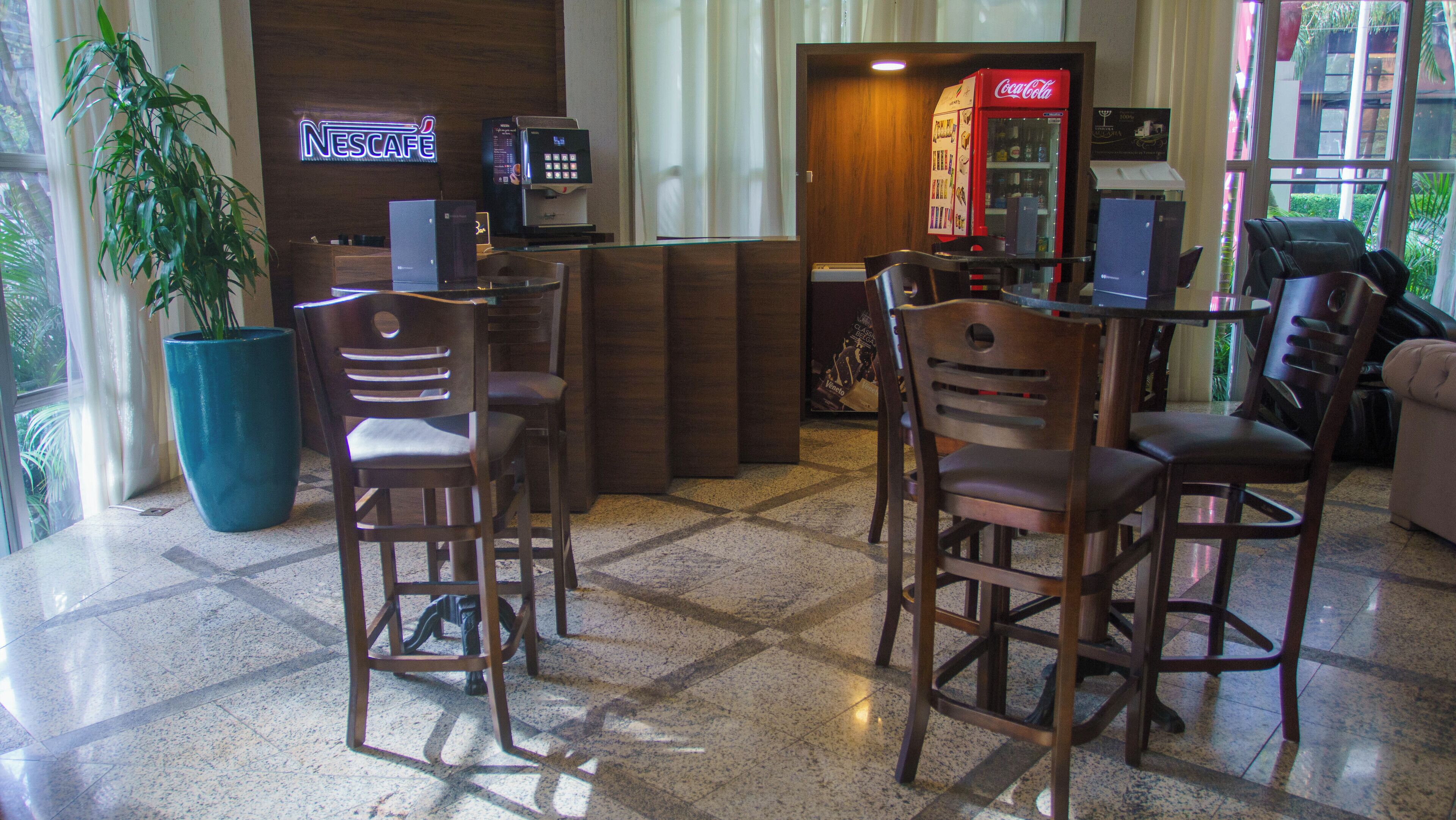 Un hall d’entrée avec une enseigne Nescafé, un distributeur automatique de Coca-Cola et une grande plante en pot.
