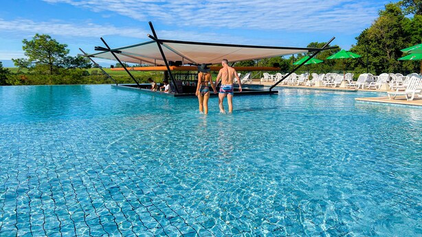 Una piscina con acqua cristallina e azzurra, circondata da lettini e ombrelloni bianchi.