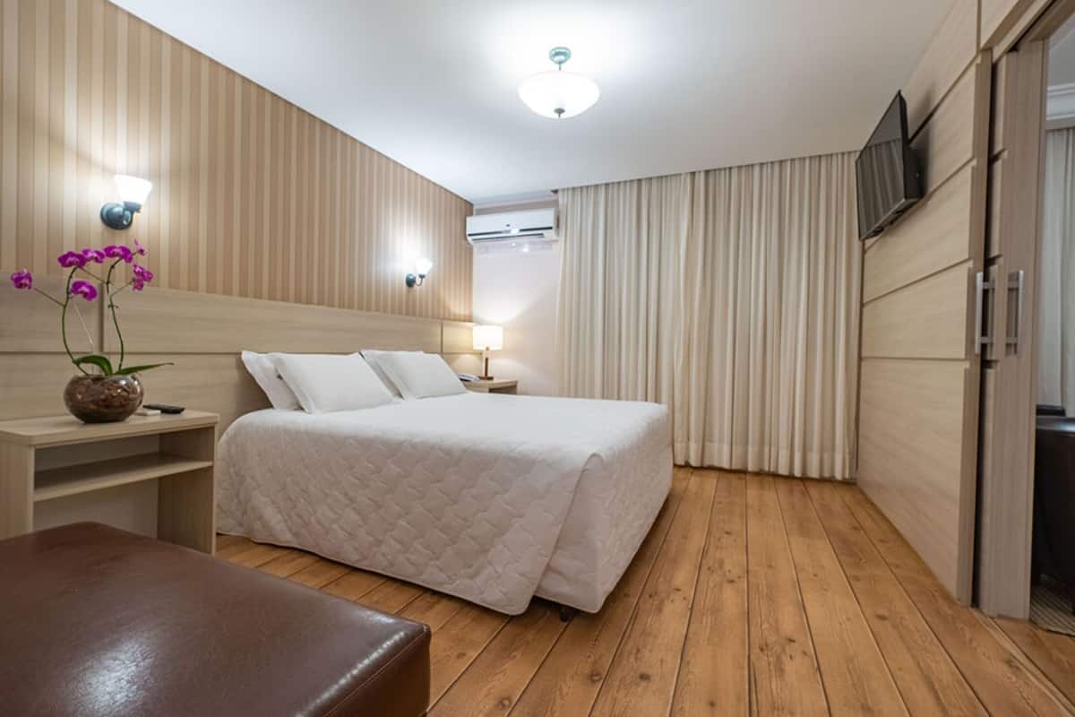Une chambre d’hôtel avec un lit, une table de chevet, un téléviseur fixé au mur et un plancher en bois.