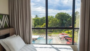 Una camera d'albergo con una grande finestra che si affaccia su una piscina e un'abbondante vegetazione.